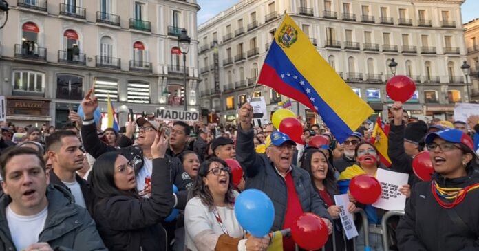 Grupo de venezolanos en una plaza europea ondeando la bandera de Venezuela y globos de colores, algunos con expresiones de júbilo, durante una manifestación relacionada con la intervención de Estados Unidos en su país.